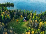 Aerial view of a red log cabin with sauna in the spring forest by a lake in Finland