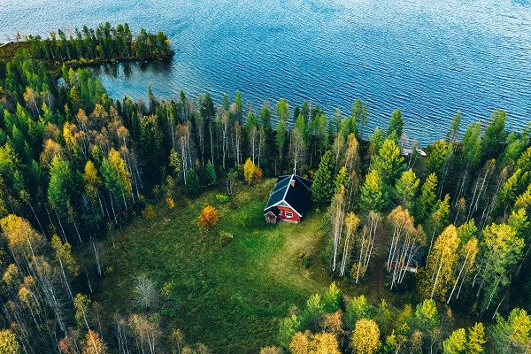 Aerial view of a red log cabin with sauna in the spring forest by a lake in Finland